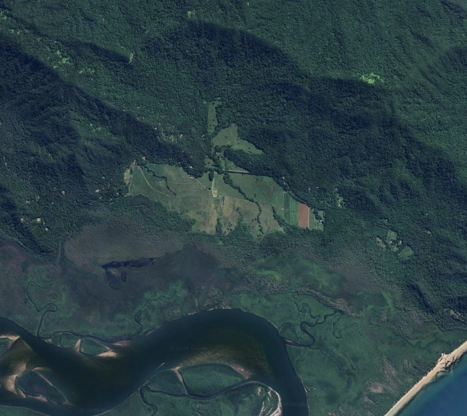 Aerial view of the Cape Kimberley station, cleared paddocks held inside rainforest, with the Daintree River below